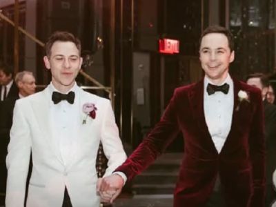 Jim Parsons and Todd Spiewak are in a tuxedo holding hands as they are walking.